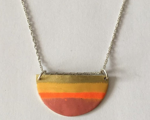 A half round shaped necklace with colorful enamel stripes, suspended from a silver chain.