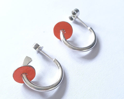 A pair of silver hoop earrings with neon orange enamel accents on the hoops, displayed against a white background.