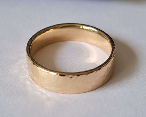 A 9ct flat hammered gold wedding ring with a light hammered and polished finish, displayed on a white surface.
