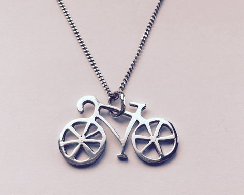 Silver bicycle pendant on a chain against a light background